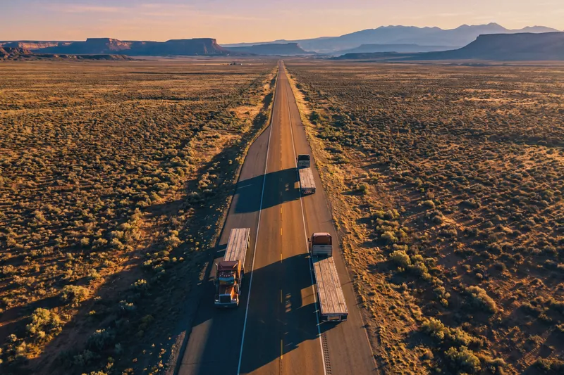 Semi-trucks on an interstate crossing open country toward distant mountains